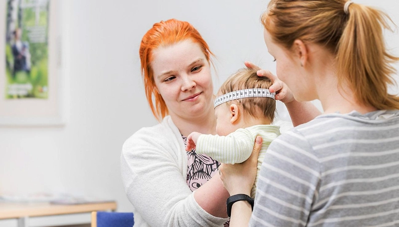 Nurse measures a child carried by their mother. - Sisä-Savon terveydenhuollon kuntayhtymä Nurse measures a child carried by their mother. - Sisä-Savon terveydenhuollon kuntayhtymä