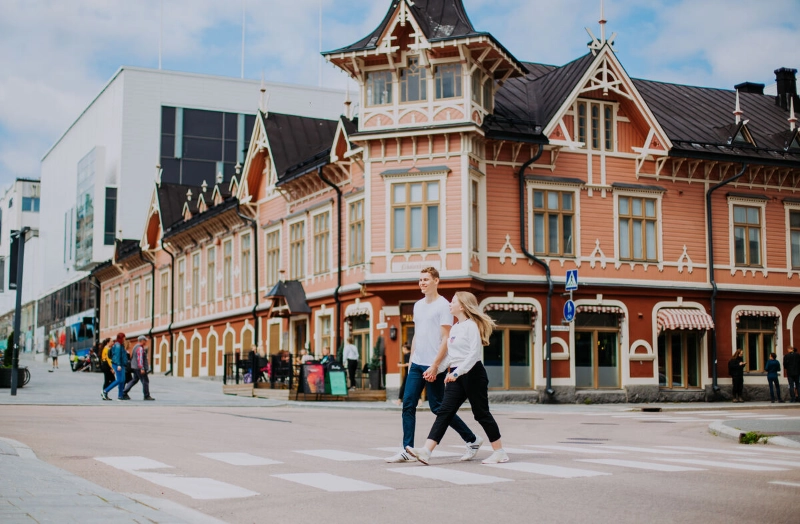 A couple crosses the street in front of a pink Victorian building. - Julia Kivelä / Finnish Lakeland /Jyväskylä Region A couple crosses the street in front of a pink Victorian building. - Julia Kivelä / Finnish Lakeland /Jyväskylä Region