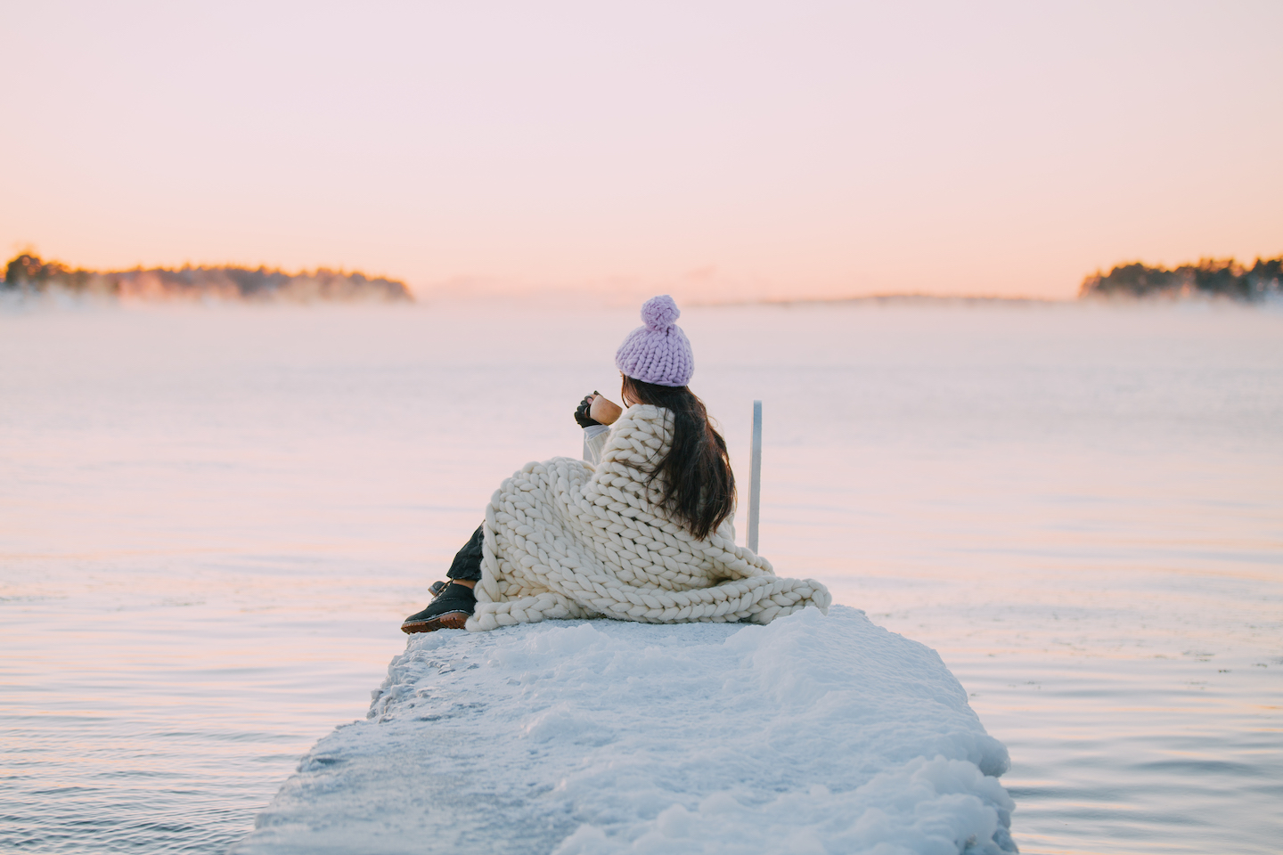 A woman sitting by a frozen dock gazing at the sea horizon in the morning light