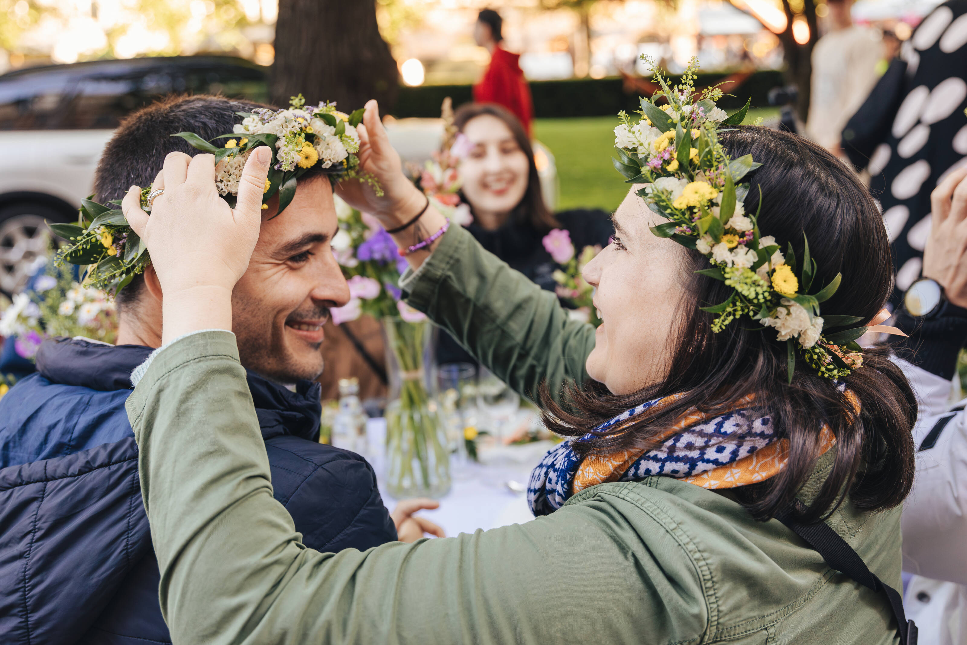 Participantes de la experiencia Helsinki Happiness Hacks, con coronas de flores, disfrutando del sol en el parque Esplanadi en Helsinki.